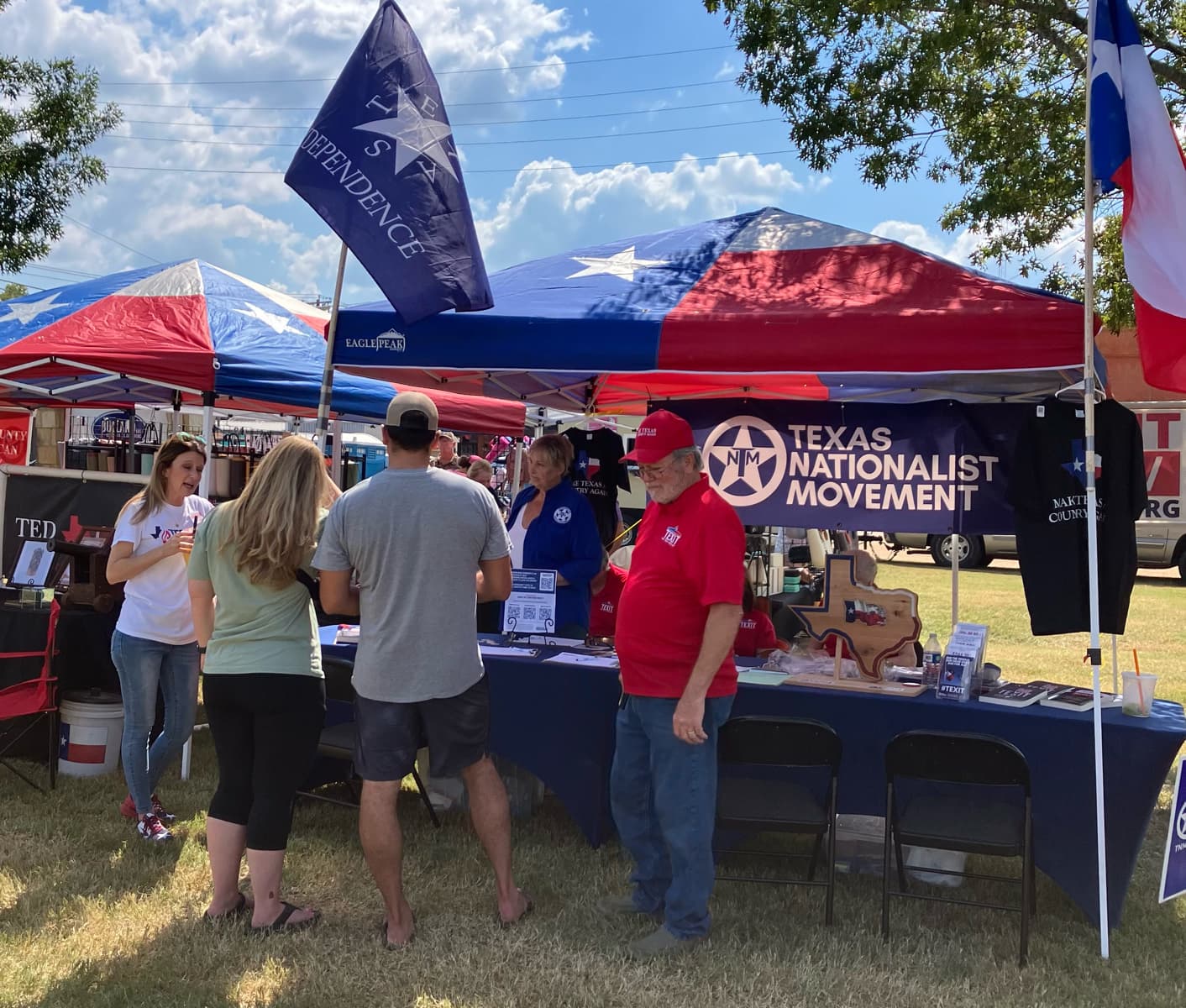 Texans gathered at a Texas Nationalist Movement booth under Texas-flag canopies at a county fair.