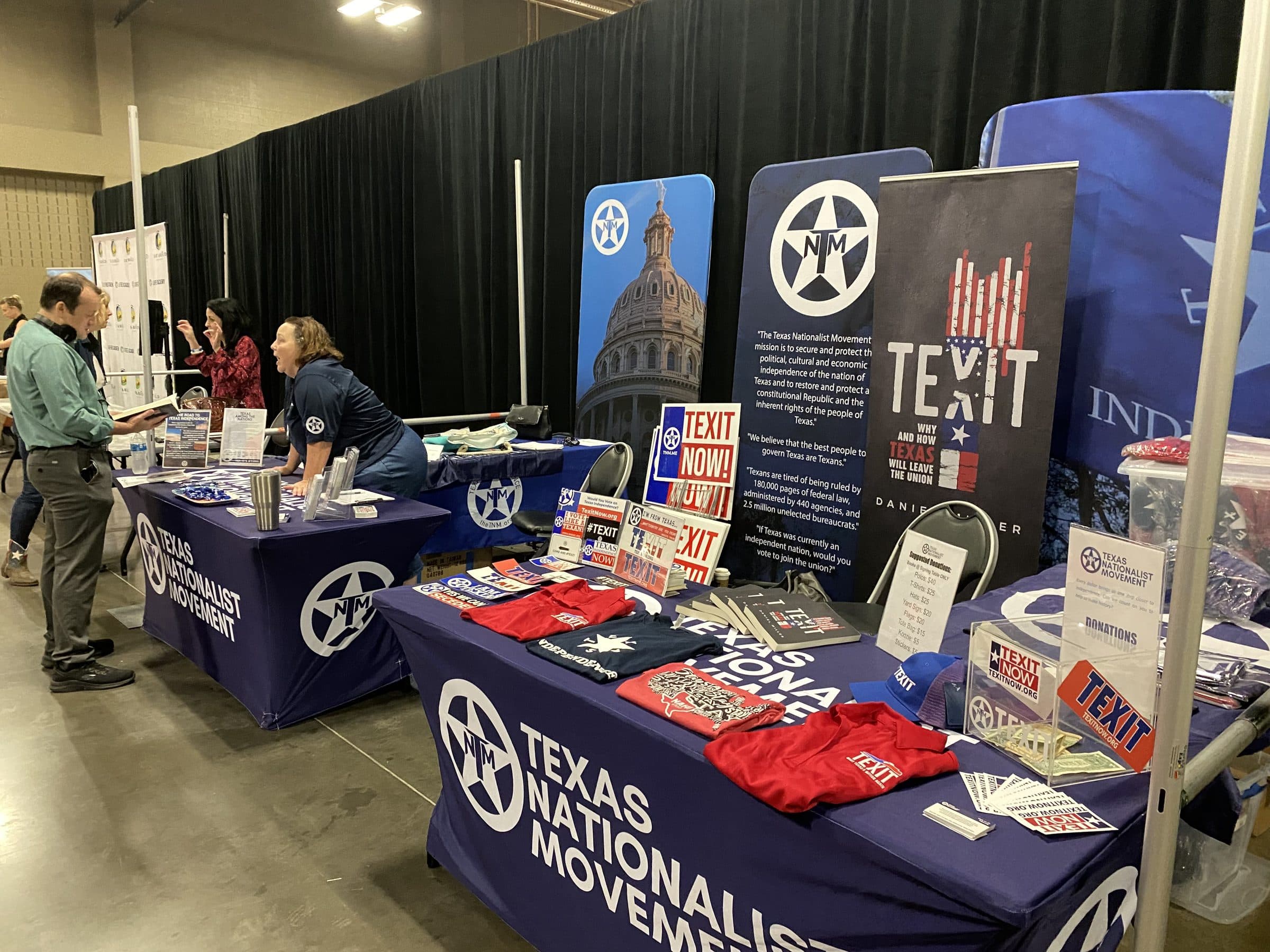 A Texas Nationalist Movement convention booth: branded banners, the TEXIT book, and staff meeting visitors.